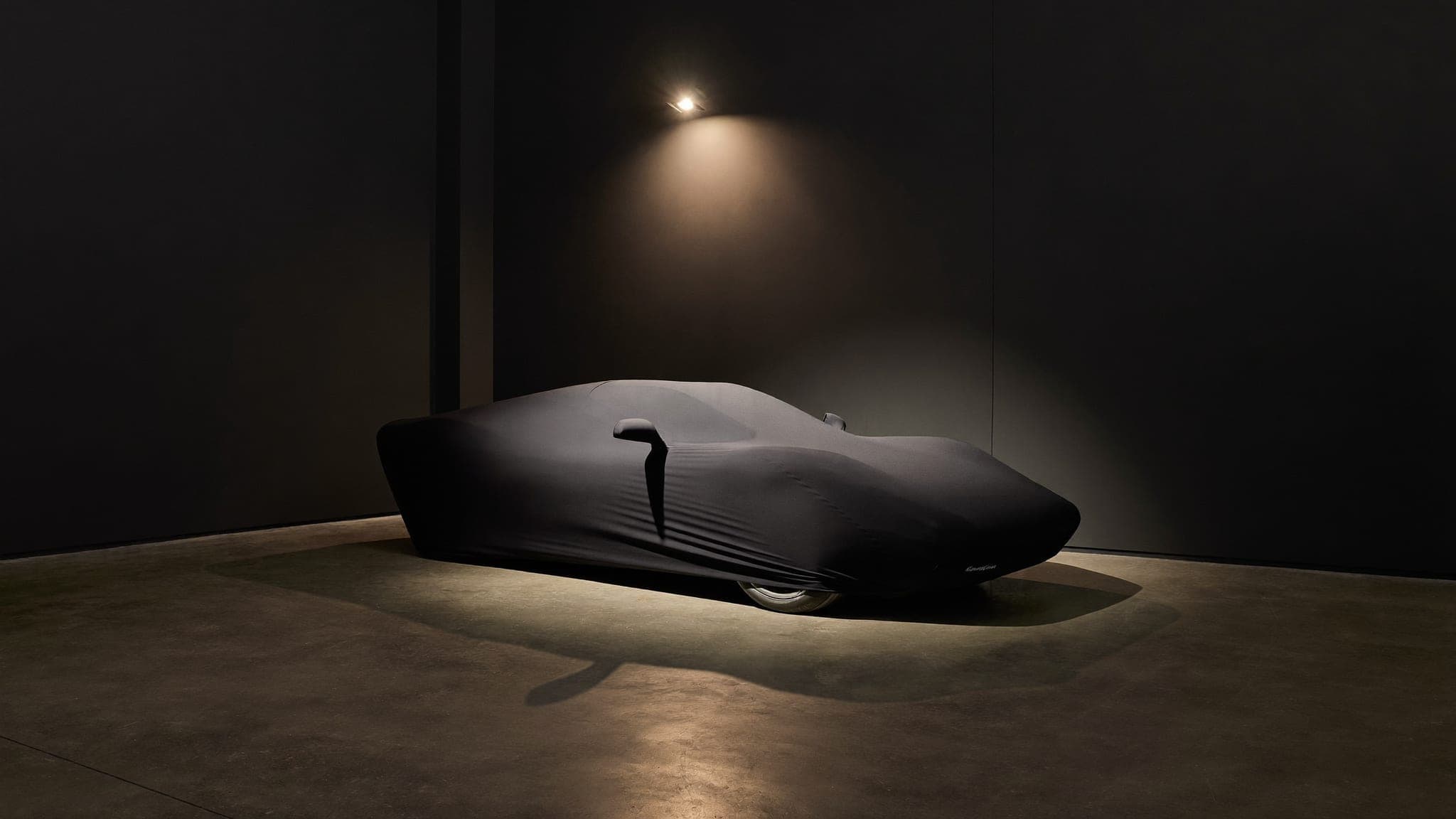 Sports car sculpturally wrapped in a fitted indoor cover under a single spotlight at Vault 620
